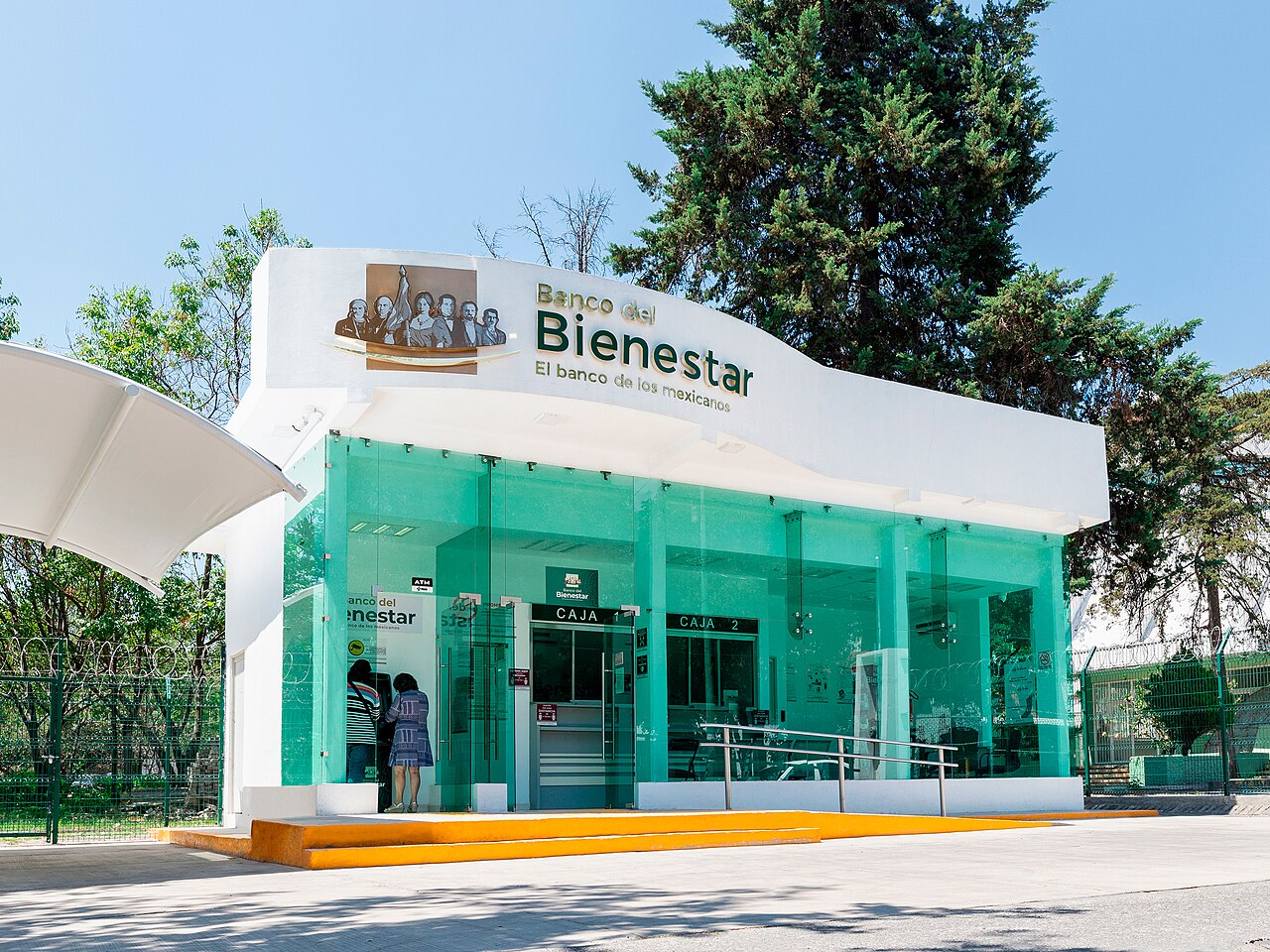 Sucursal del Banco del Bienestar en la Ciudad de México: fachada blanca con cristales verdes y una persona frente al cajero automático
