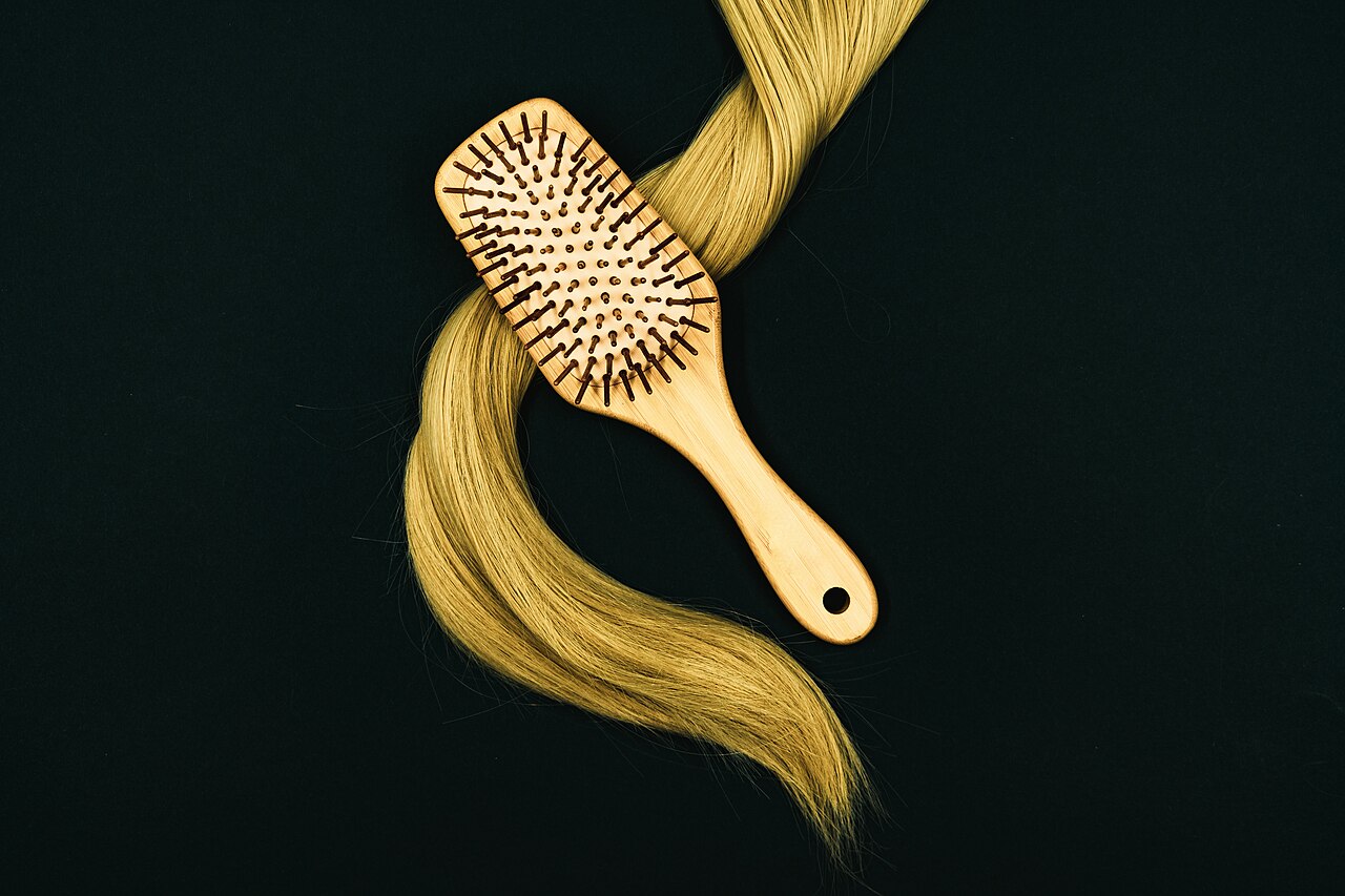 Un cepillo de madera sobre una mecha de cabello rubio, sobre fondo oscuro