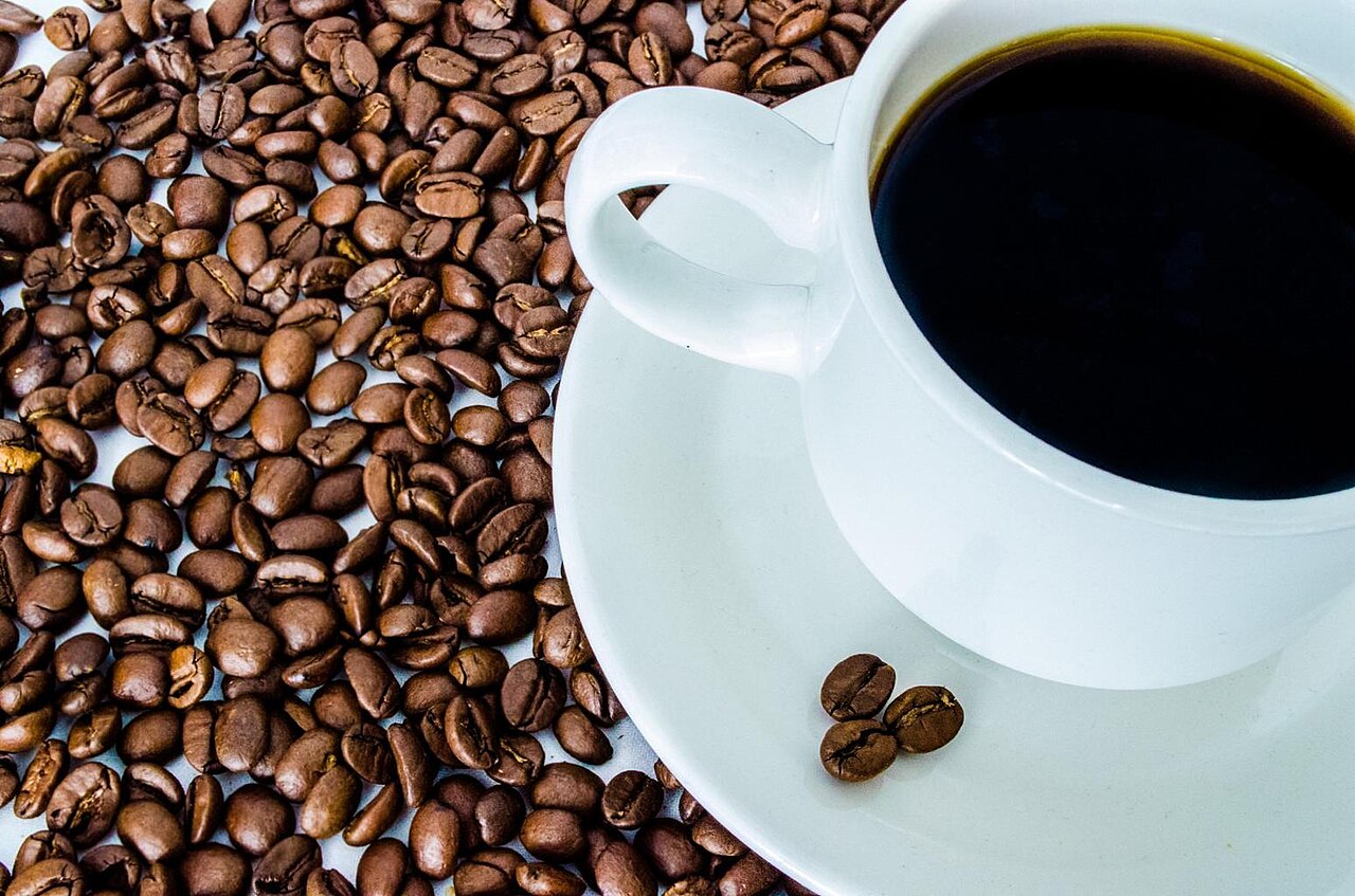 Una taza blanca con café negro sobre un platillo, rodeada de granos de café tostado