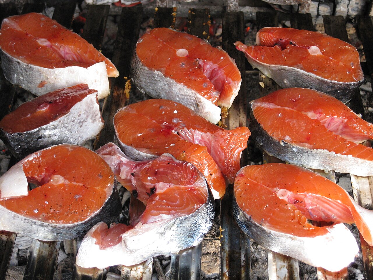 Filetes de salmón crudo colocados sobre una parrilla de carbón, listos para asar