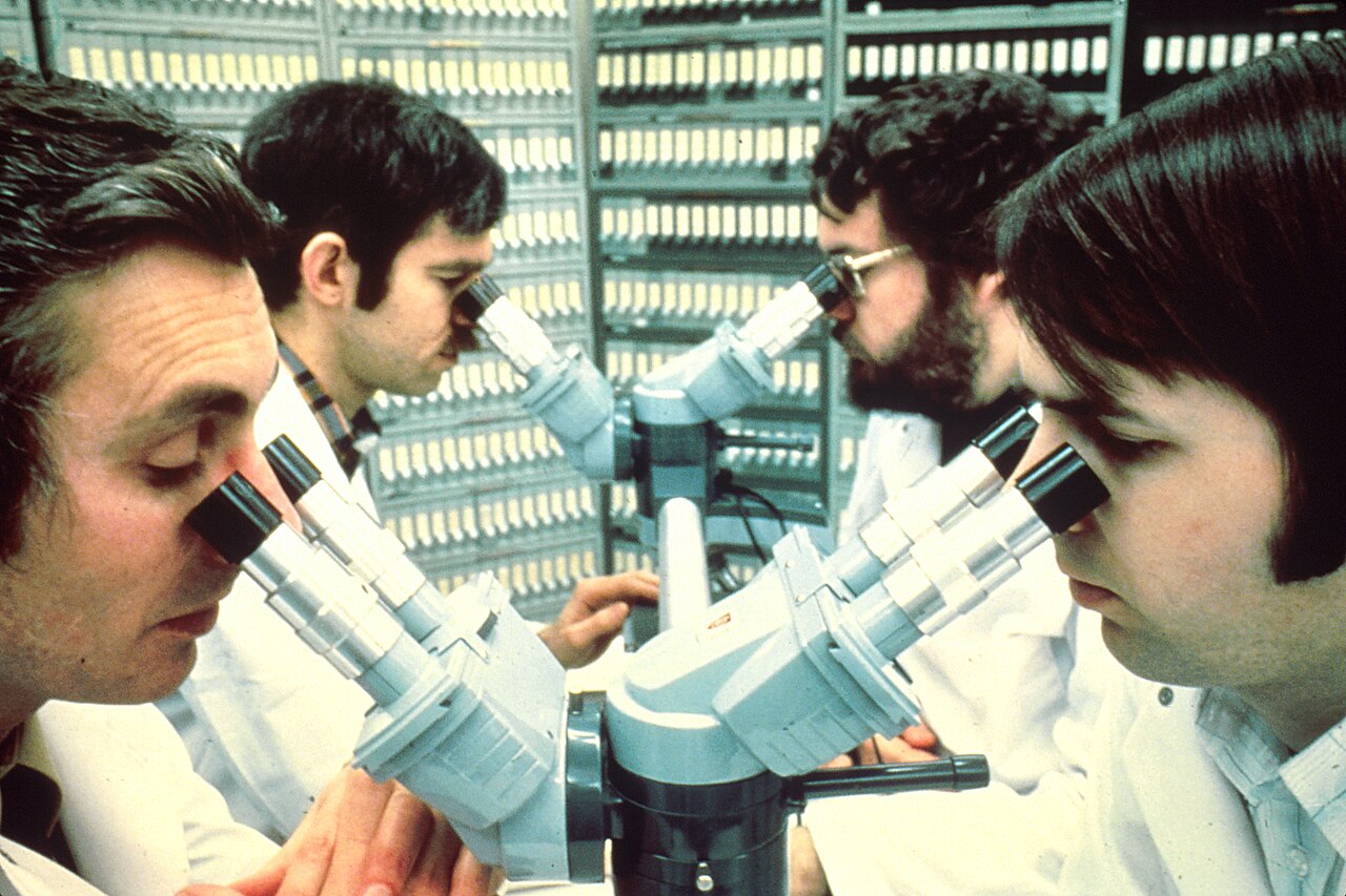 Cuatro patólogos con bata blanca observan muestras a la vez a través de un microscopio de cuatro cabezales