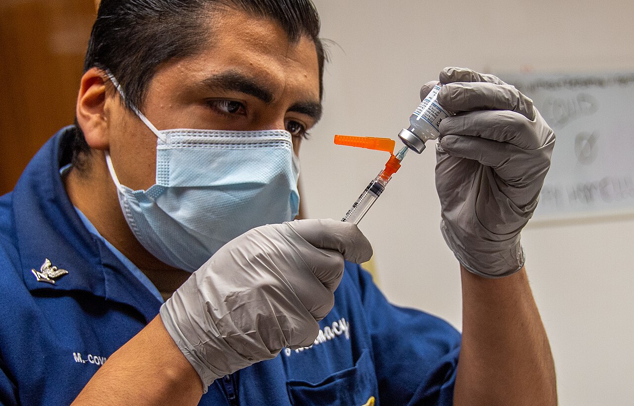 Un sanitario con mascarilla y guantes carga una jeringa con vacuna desde un vial