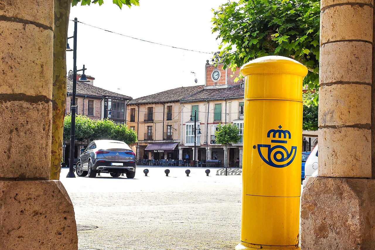 Buzón amarillo de Correos con el logotipo de la empresa en la plaza Mayor de Villadiego