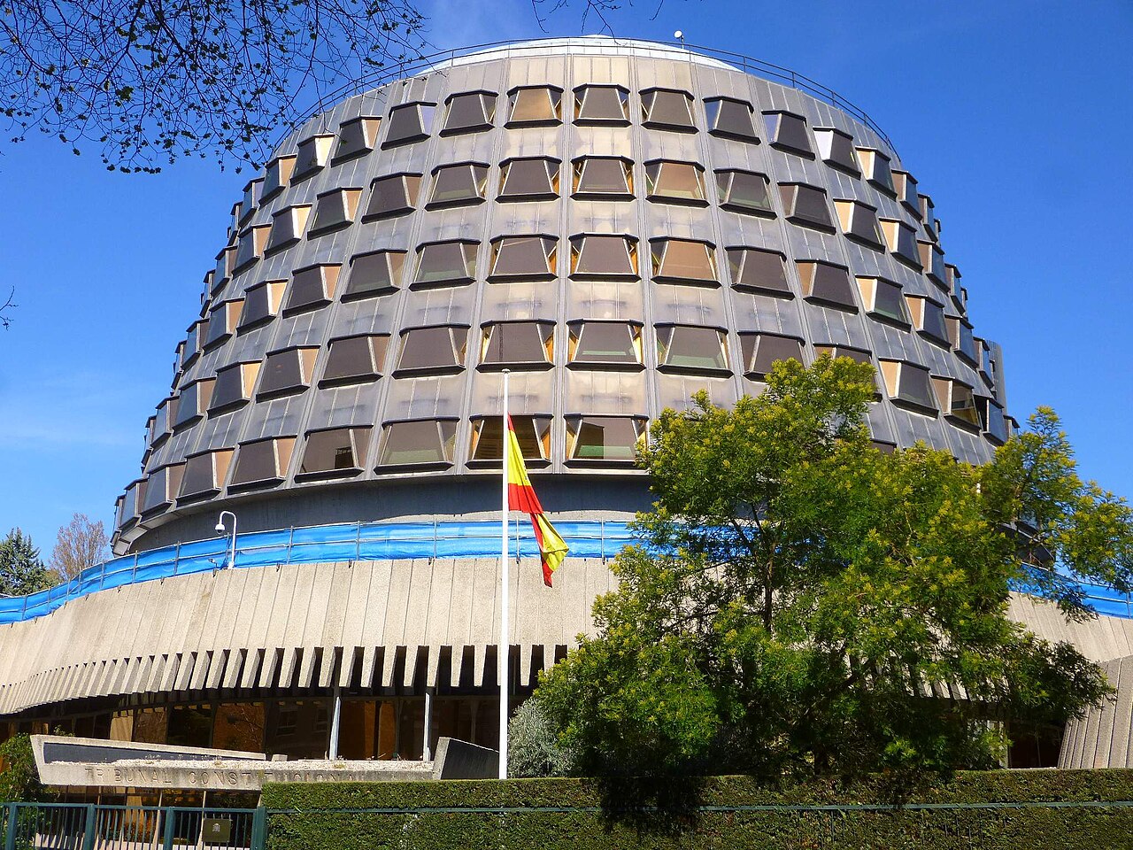 Fachada circular de la sede del Tribunal Constitucional de España en Madrid, con una bandera española en primer plano