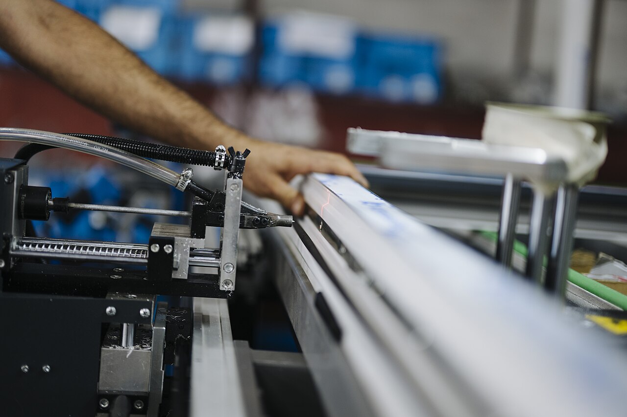 Las manos de un operario guían un perfil metálico en una máquina de una línea de producción industrial