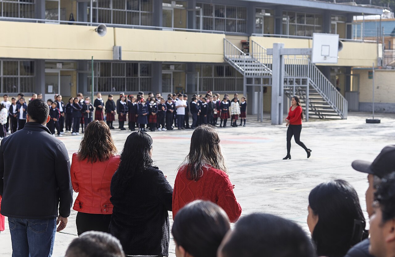 Alumnos de una primaria formados en el patio durante la ceremonia de inicio de ciclo escolar en la Ciudad de México, con madres y padres de espaldas en primer plano