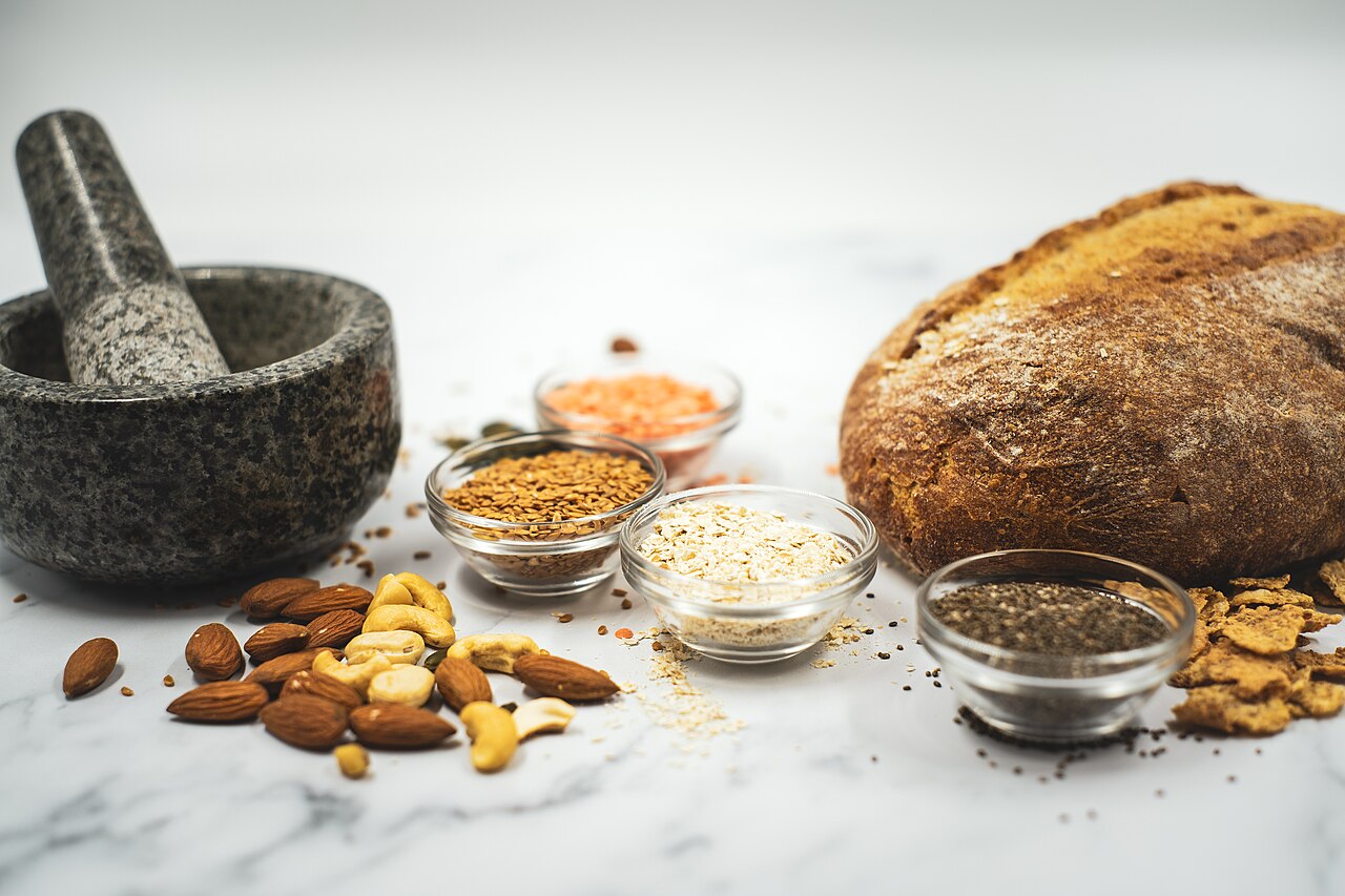 Pan de masa madre, almendras, anacardos y cuencos con semillas y granos sobre una encimera de mármol blanco